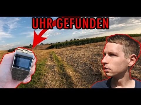 Ein Mann steht an einem Feldweg und Maisfeldern, während eine Hand eine mit einem roten Pfeil markierte Digitaluhr hält. Großer roter Text sagt UHR GEFUNDEN und erinnert an den Nervenkitzel von Schatzsuche metalldetektor Abenteuern.