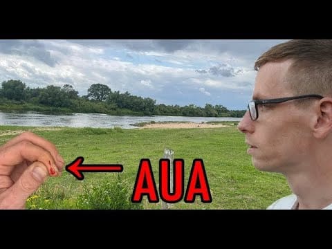 Eine Person mit Brille blickt auf eine Hand mit einer kleinen blutenden Wunde am Finger, auf die ein roter Pfeil und "AUA" in fetter Schrift hinweisen. Ein Fluss und eine grasbewachsene Landschaft erinnern an Szenen von Schatzsuche metalldetektor-Abenteuern.