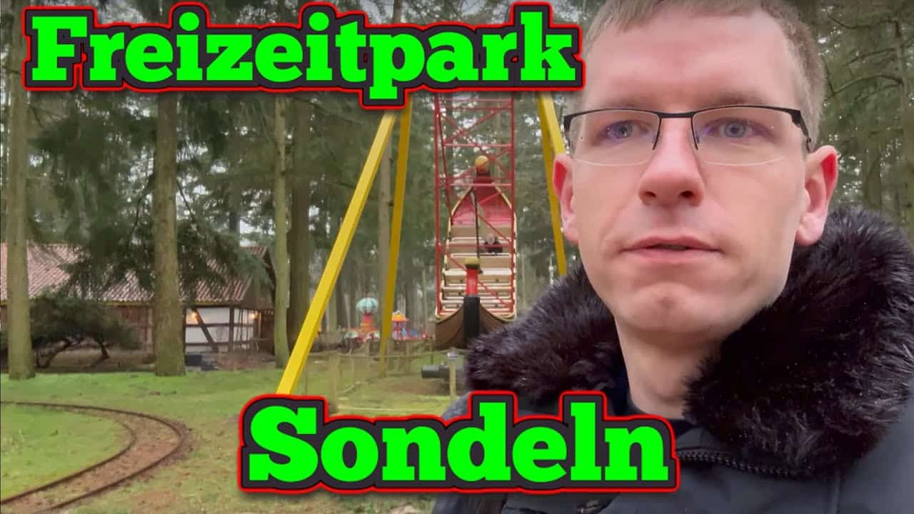 Ein Mann mit Brille steht vor einem bewaldeten Vergnügungspark, hinter ihm sind eine kleine Bahnstrecke und ein Fahrgeschäft zu sehen. Die Worte Freizeitpark Sondeln sind in fetter grüner und roter Schrift eingeblendet, als ob er etwas im See verloren hätte.