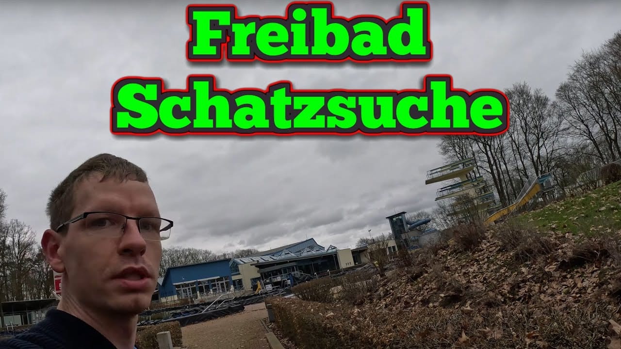 Ein Mann mit Brille steht an einem bewölkten Tag vor einem Freibadkomplex. Oben erscheint der große deutsche Text Freibad Schatzsuche, der auf eine Veranstaltung der Schatzsuche Metalldetektor hinweist. Das Gelände ist von kahlen Bäumen umgeben.