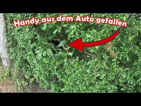 Ein Smartphone ist im grünen Gebüsch zu sehen, hervorgehoben durch einen roten Kreis und einen Pfeil. Der deutsche Text darüber lautet "Handy aus dem Auto gefallen" - perfekt für Momente, in denen der Ring verloren gegangen ist oder die Schatzsuche metalldetektor.