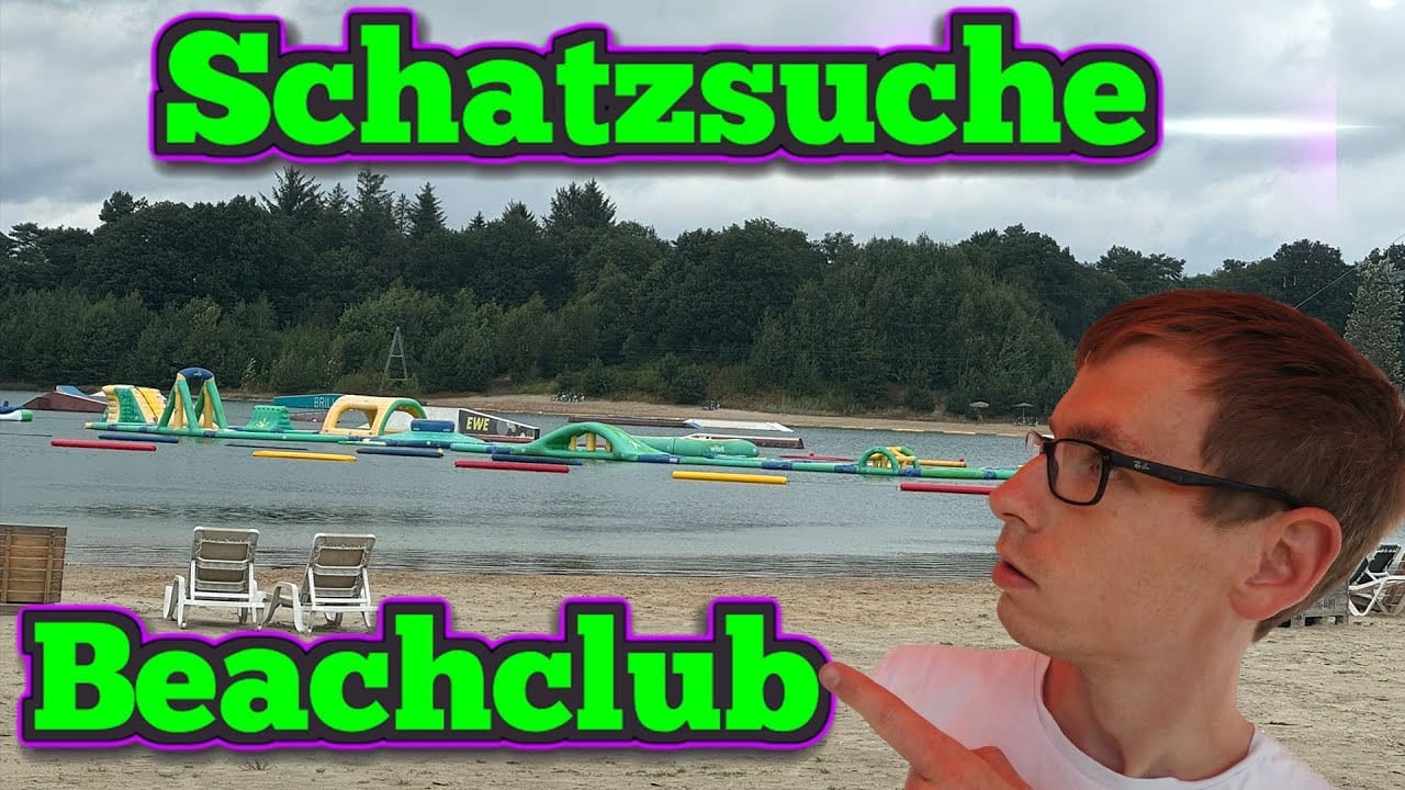 Ein Mann mit Brille zeigt auf einen aufblasbaren Hindernisparcours auf einem See - perfekt für ein "Schatzsuche"-Abenteuer. Oben steht fett "Schatzsuche" und unten "Beachclub", was auf "Schätze im See verloren" hindeutet. Der Hintergrund ist mit Bäumen bepflanzt.