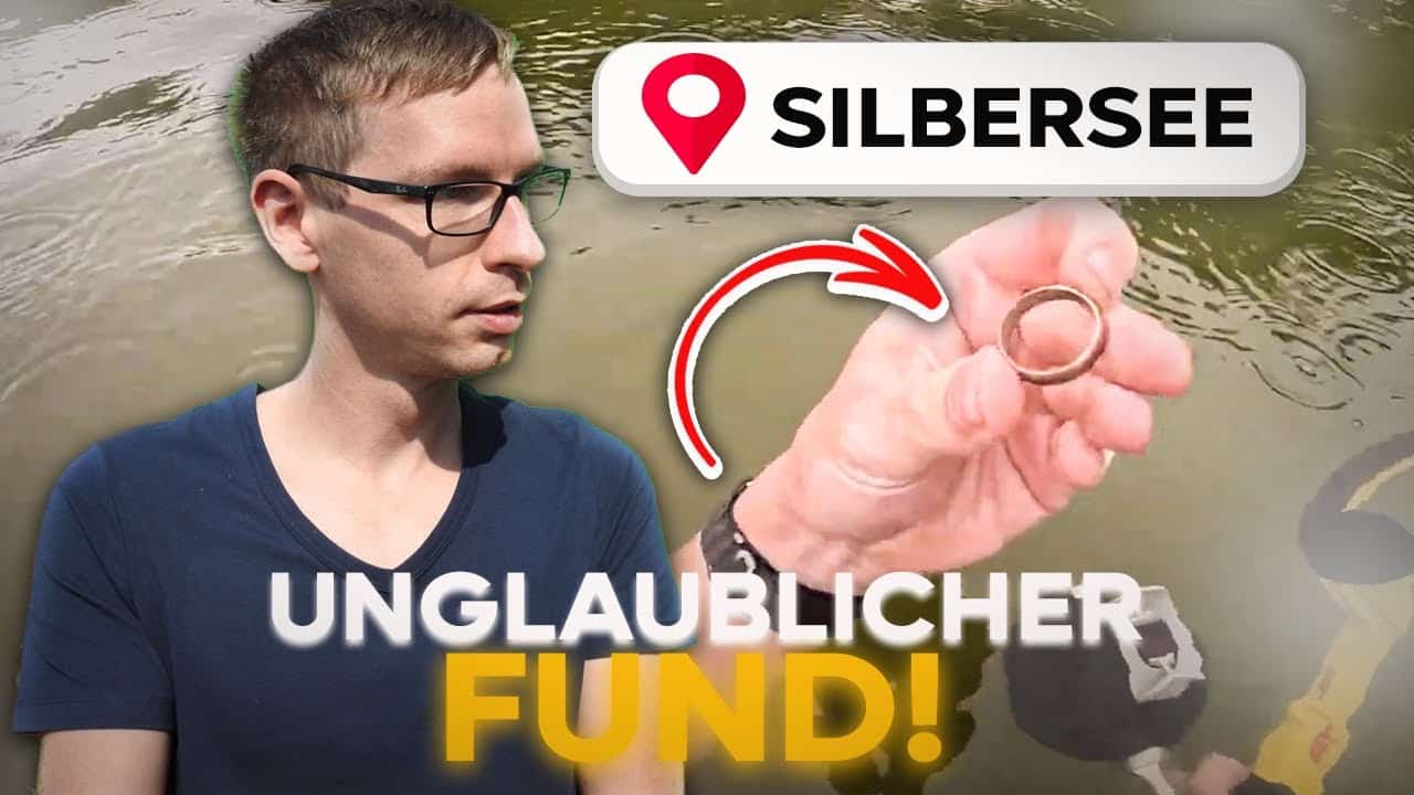 Ein Mann blickt auf eine Hand, die einen Ring über Wasser hält. Der Text lautet SILBERSEE mit einem Stecknadelsymbol und UNGLAUBLICHER FUND! mit einem Pfeil auf den Ring. Menschen suchen den See im Hintergrund ab - obwohl der Ring im See verloren war, wurde er gefunden!.