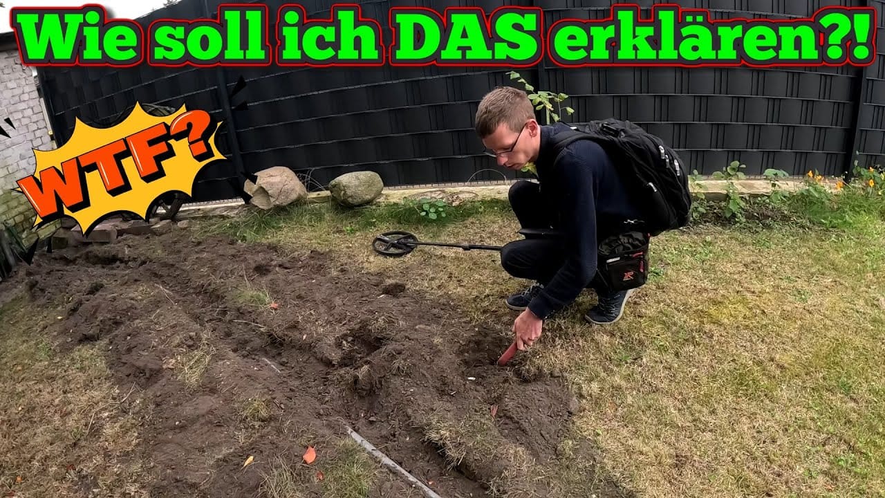 Ein Mann mit einem Rucksack benutzt eine Schatzsuche Metalldetektor und ein kleines Grabungswerkzeug in einem schmutzigen Bereich. Der Text darüber lautet "Wie soll ich DAS erklären?!" und "WTF?" in bunten, fetten Buchstaben. Im Hintergrund sind ein schwarzer Zaun und einige Felsen zu sehen.
