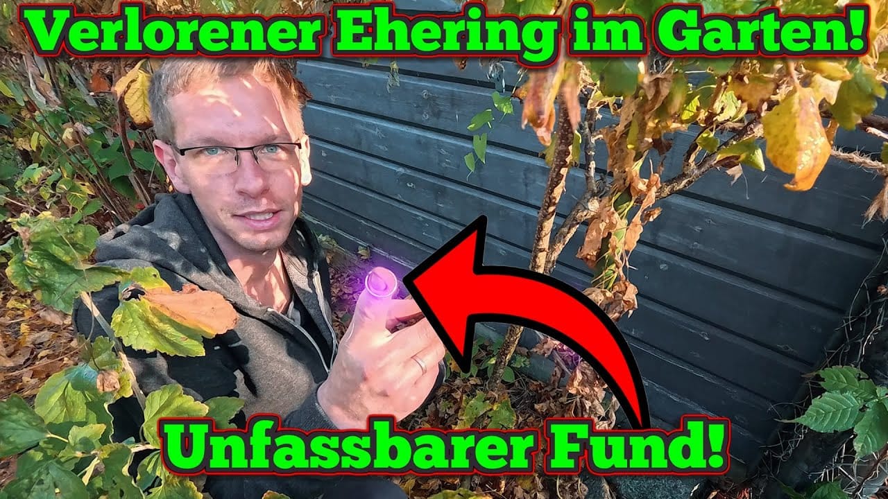 Ein Mann mit einem violetten Gegenstand kniet neben Büschen und einem Zaun. Der deutsche Text lautet Verlorener Ehering im Garten! Schatzsuche Metalldetektor! mit einem roten Pfeil, der auf das Objekt zeigt.