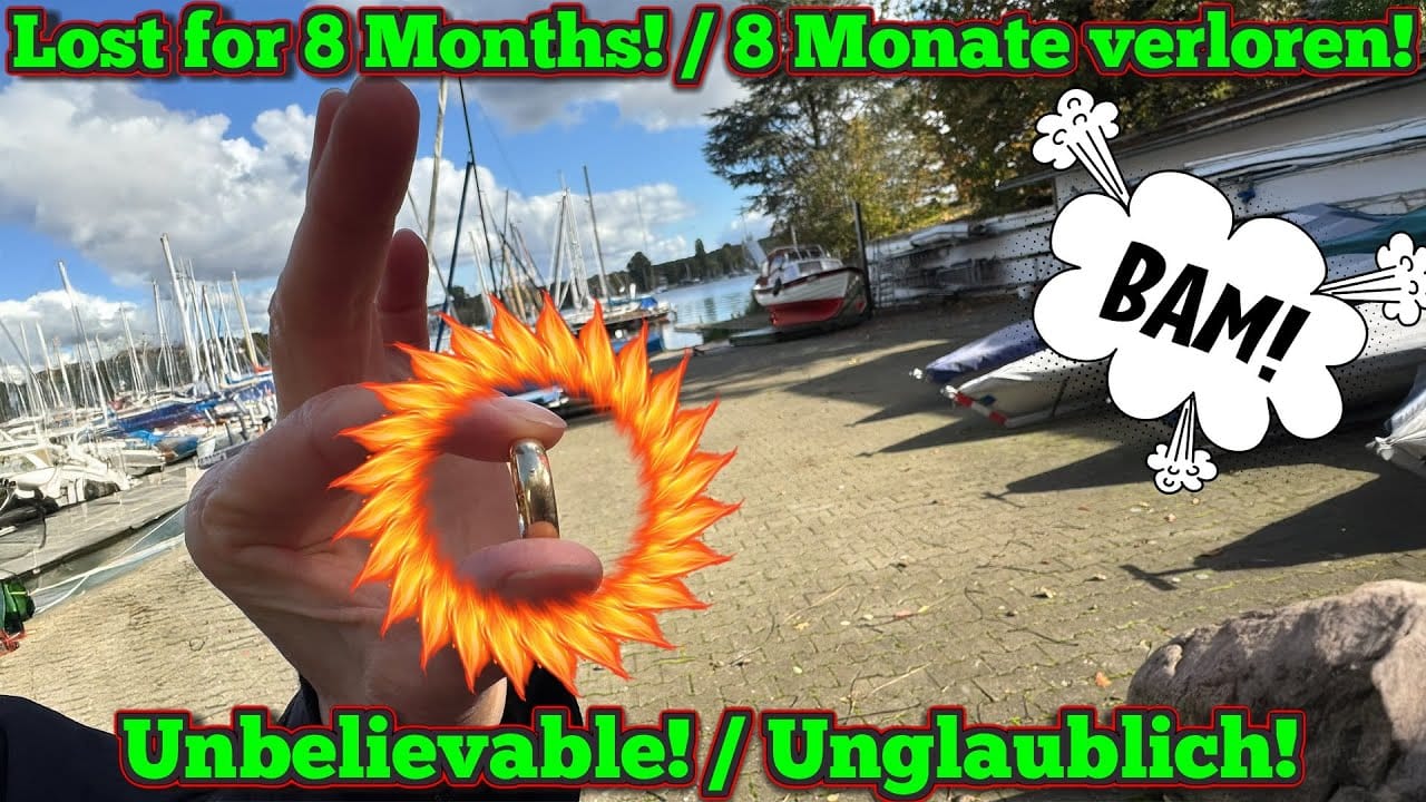 Eine Hand hält einen goldenen Ring mit einer feurigen Grafik in der Nähe eines Jachthafens, Boote im Hintergrund. Der fettgedruckte Text lautet "Lost for 8 Months!" und "Unbelievable!" - plus die Comic-Grafik "BAM!". "Im See verloren" unterstreicht die dramatische Geschichte auf Englisch und Deutsch.