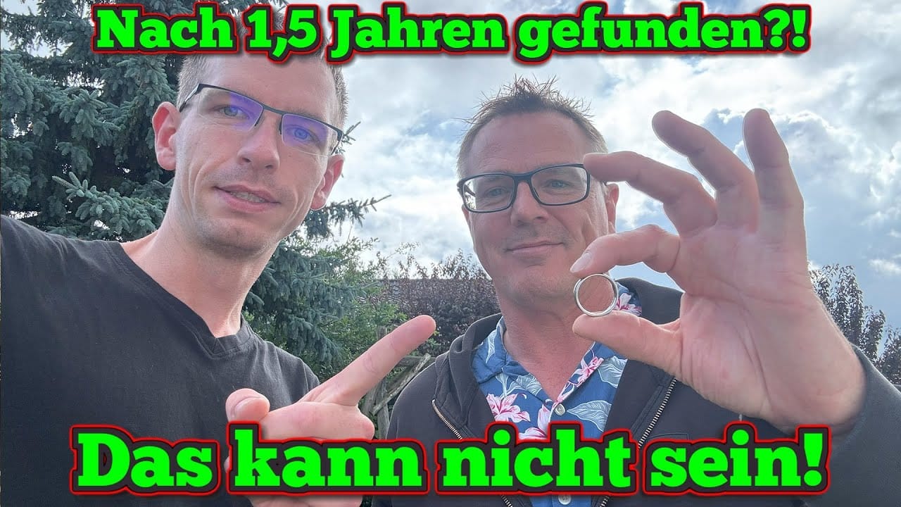 Zwei Männer stehen im Freien unter einem wolkenverhangenen Himmel. Der eine hält einen Ring hoch, der andere zeigt auf ihn - nach einer Schatzsuche Metalldetektor. Oben steht in grüner und roter Schrift: "Nach 1,5 Jahren gefunden?!" und unten: "Das kann nicht sein!.